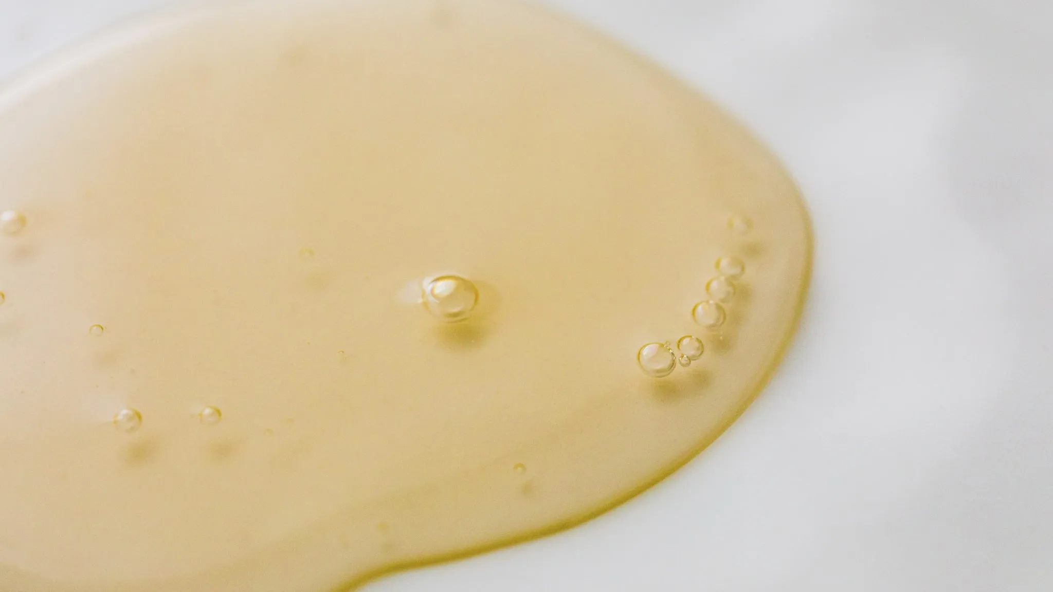 Een plas doorschijnende gele olie van bovenaf gefotografeerd, met kleine luchtbelletjes aan de rand.