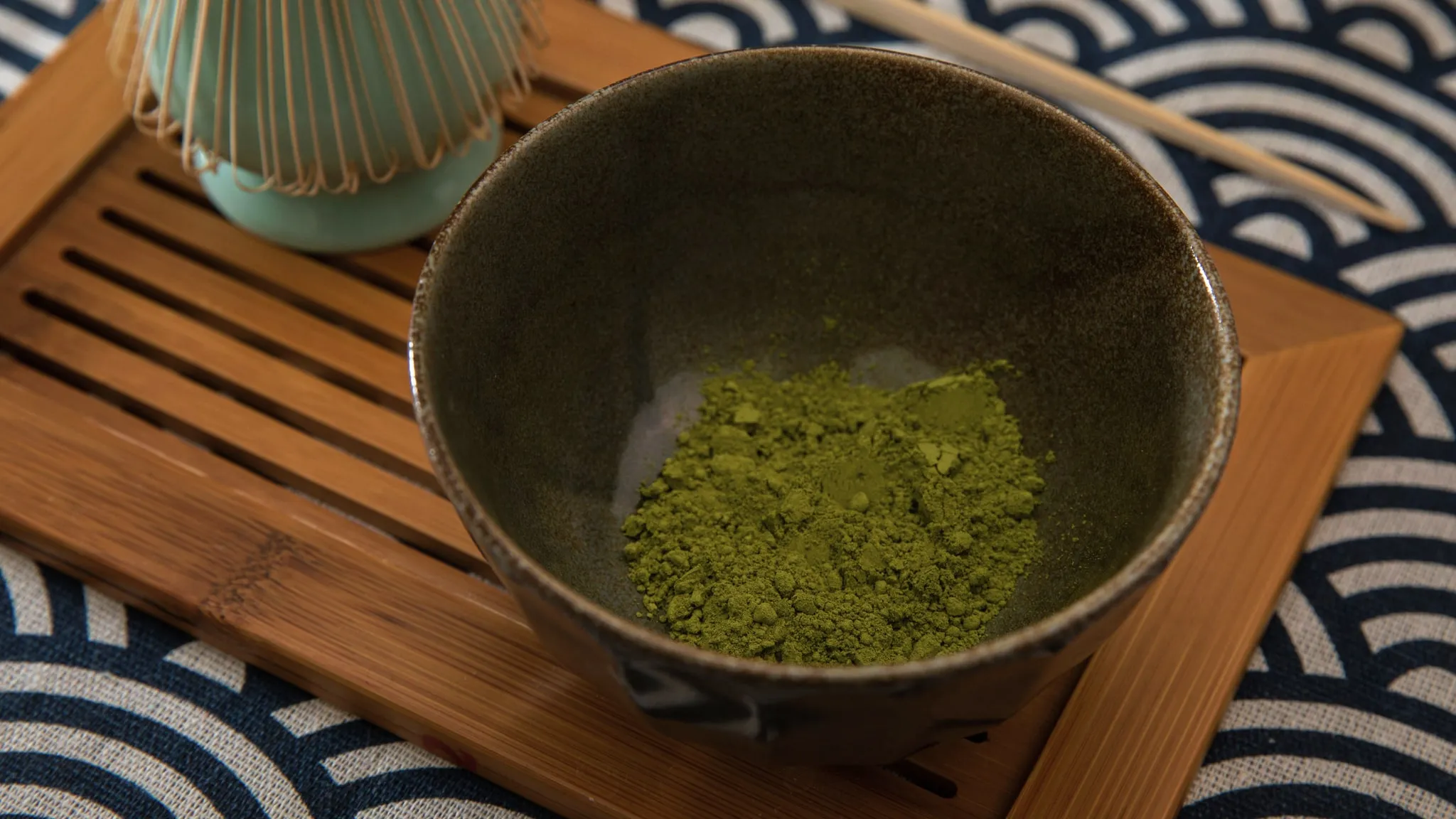 Losse gedroogde groene thee opgehoopt in een klein keramieken schepje op linnen.