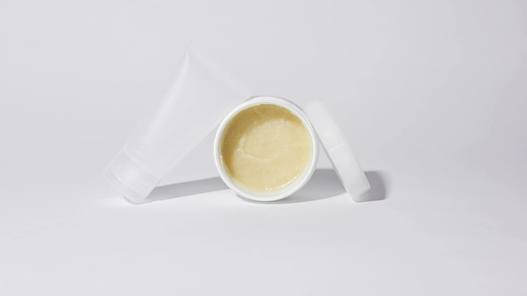 Een geopend potje met een gladde balm, minimaal gefotografeerd op een witte ondergrond.