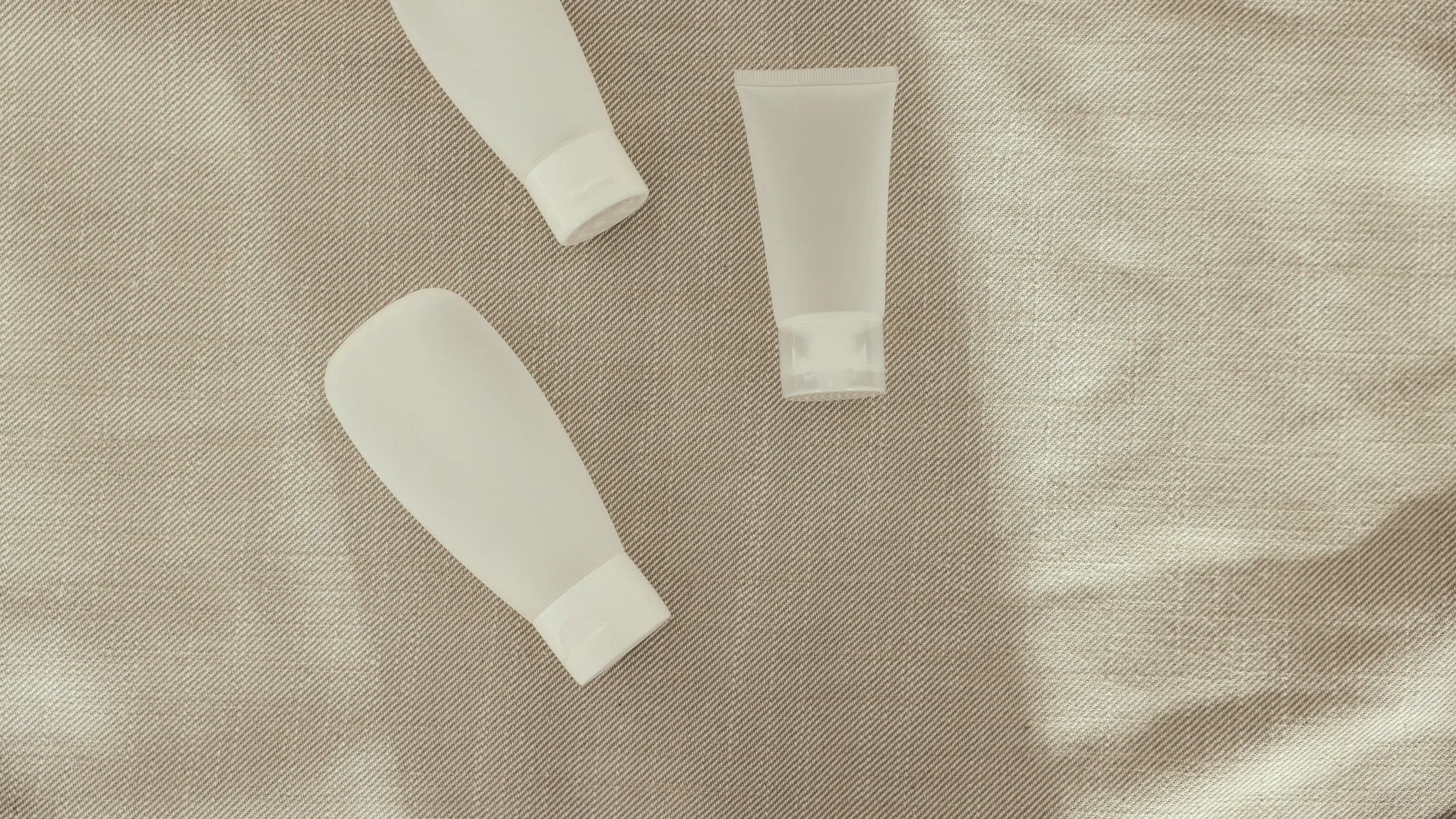 Twee witte tubes zonder etiket, liggend op een ongebleekt linnen doek.