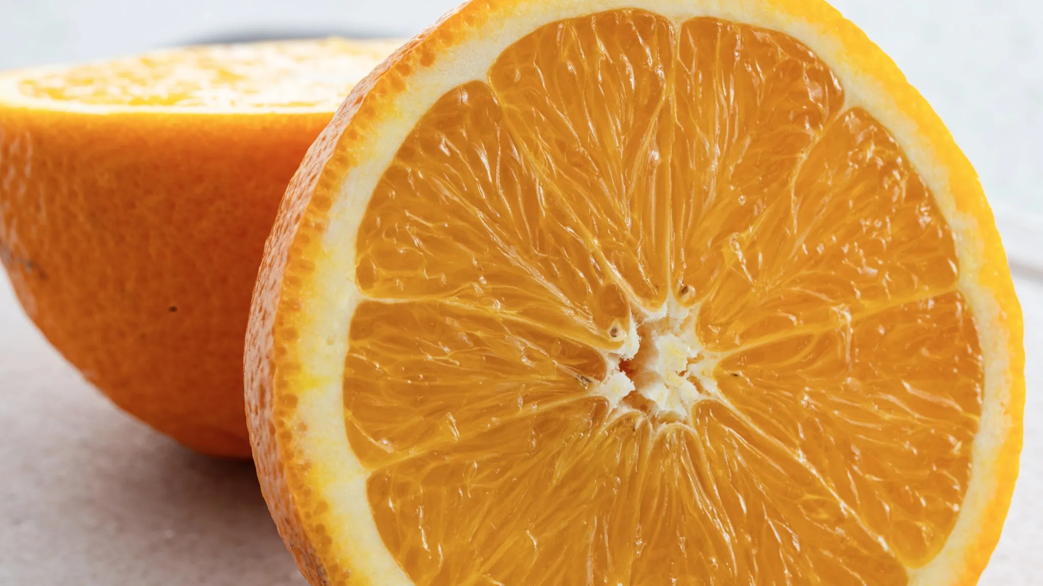 Een doorgesneden citrusvrucht, macro, met de partjes doorschijnend, van achteren belicht tegen een lichte achtergrond.
