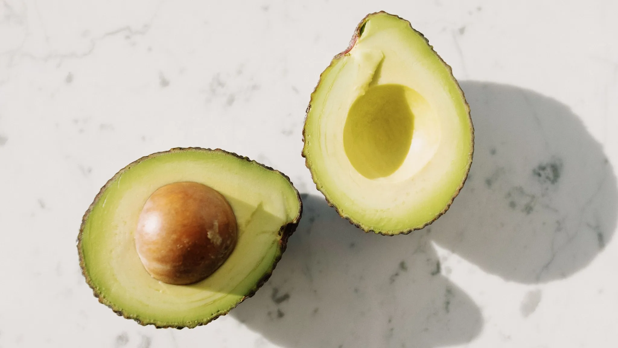 Een doorgesneden avocado op een houten plank, het vruchtvlees vangt het licht.