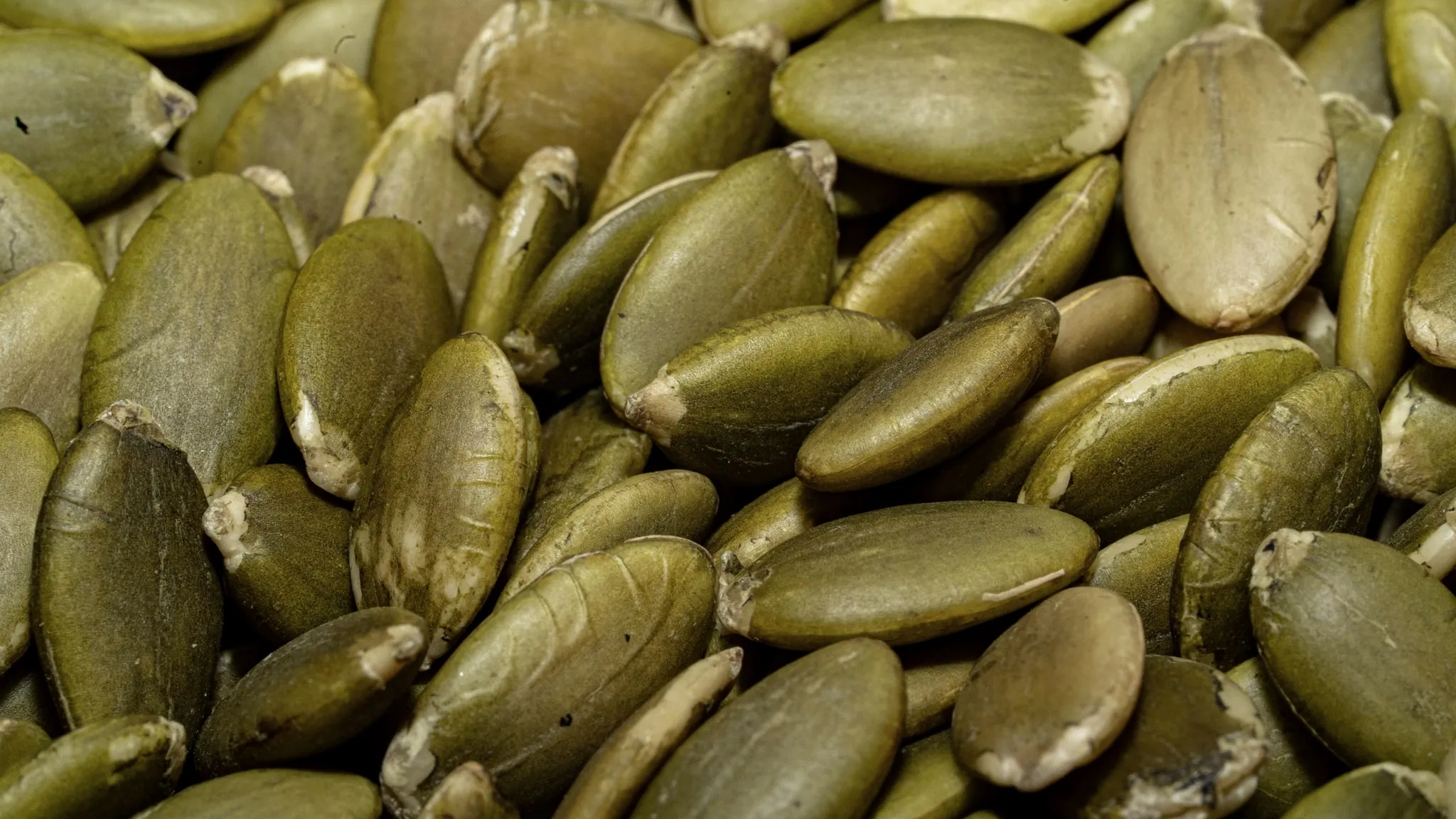 Pompoenpitten en cashewnoten uit een papieren zak, uitgestrooid op licht linnen.
