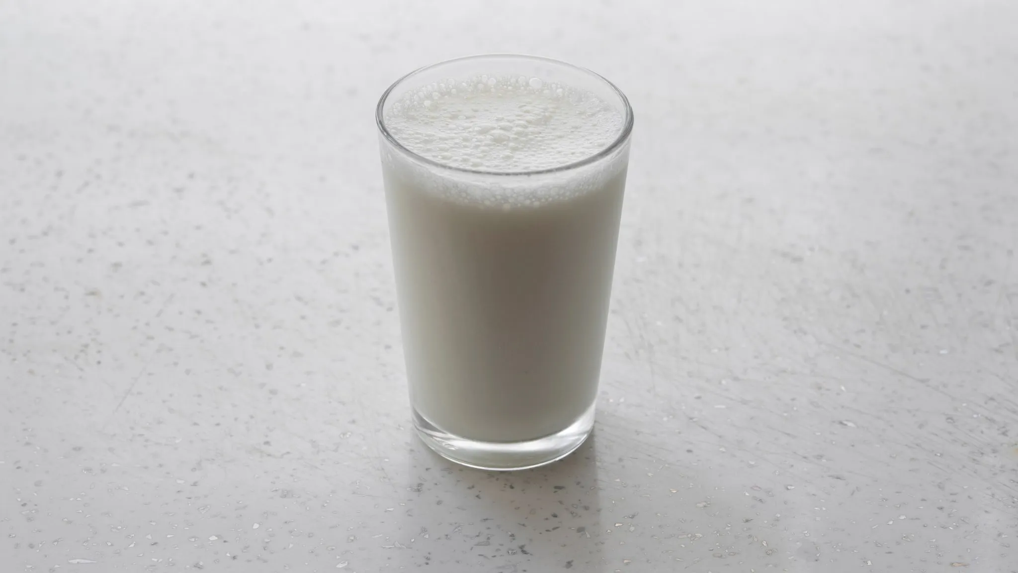 Een eenvoudig glas melk op een lichte tafel in sterk zijlicht, met geringe scherptediepte.